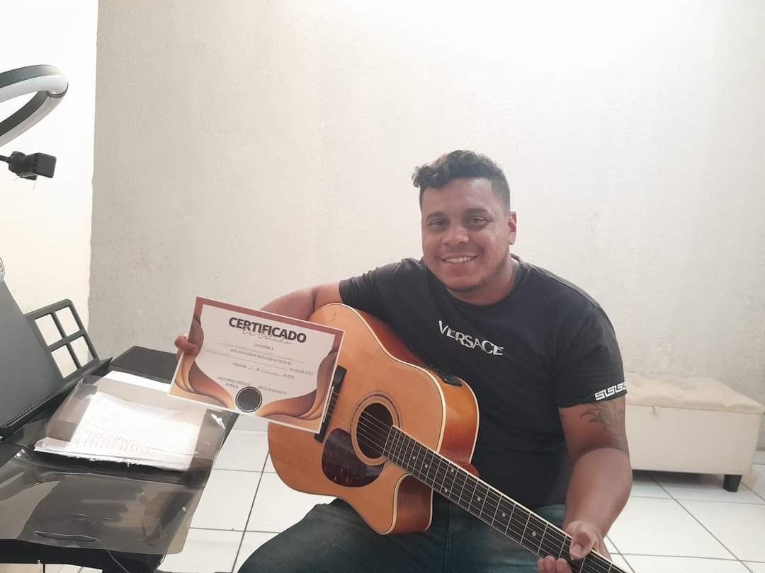 Aluno adulto com o violão no colo mostrando o certificado do curso
