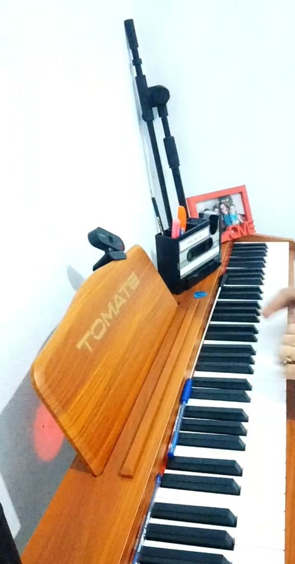 Piano digital Tomate de madeira alaranjada com um porta-canetas em forma de fita cassete e uma webcam em cima